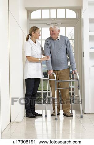 Stock Image - Carer Helping Elderly Senior Man Using Walking Frame. Fotosearch