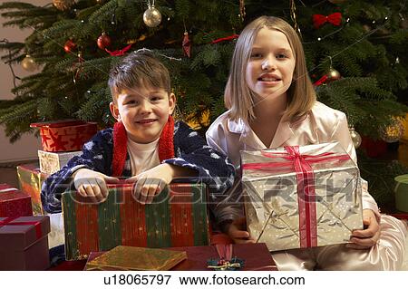 Stock Photo - Children Opening Christmas Present In Front Of Tree. Fotosearch