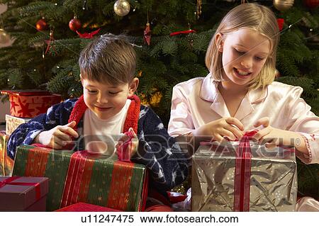 Stock Photography - Children Opening Christmas Present In Front Of Tree. Fotosearch