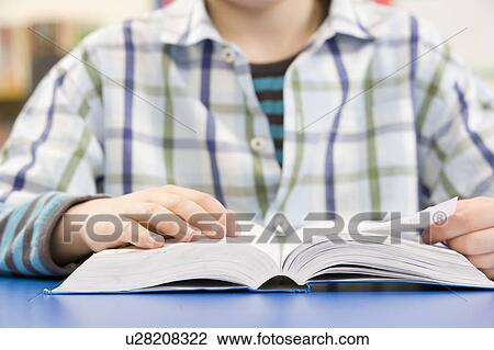 Stock Image - Close Up Of Schoolboy Studying Textbook In Classroom. Fotosearch