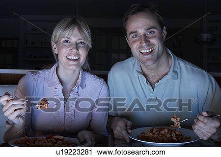 Stock Image - Couple Enjoying Meal Whilst Watching TV. Fotosearch