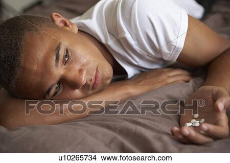 Picture - Depressed Teenage Boy Lying In Bedroom With Pills. Fotosearch