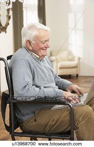 Stock Image - Disabled Senior Man Sitting In Wheelchair Using Laptop. Fotosearch