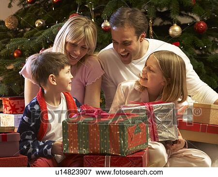 Stock Photo - Family Opening Christmas Present In Front Of Tree. Fotosearch