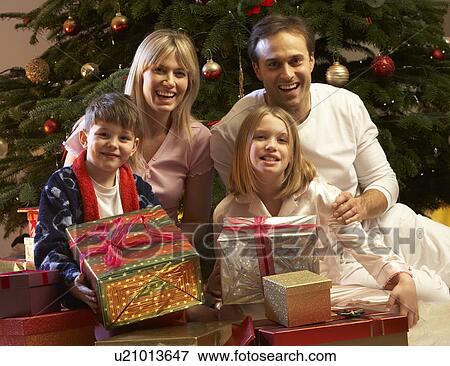 Stock Photo - Family Opening Christmas Present In Front Of Tree. Fotosearch