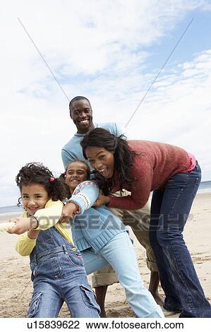 Stock Image - Family playing tug of war on beach. Fotosearch