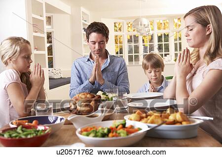 Stock Image - Family Saying Prayer Before Eating Roast Dinner. Fotosearch