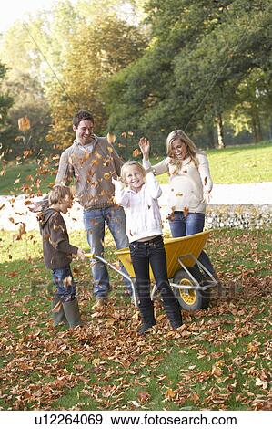Stock Photo - Family throwing autumn leaves into the air in garden. Fotosearch