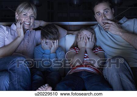 Stock Image - Family Watching Scary Programme On TV Sitting On Sofa Together. Fotosearch