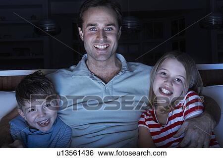 Stock Photograph - Father And Children Watching Programme On TV Sitting On Sofa Together. Fotosearch