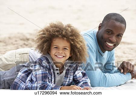 Picture - Father and son laying on beach. Fotosearch