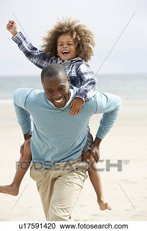 Stock Image - Father and son playing piggyback on beach. Fotosearch