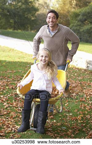 Father pushing child through autumn leaves on wheelbarrow View Large Photo Image Stock Photo - Father pushing child through autumn leaves on wheelbarrow. Fotosearch