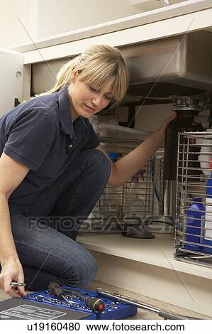 Stock Image - Female Plumber Working On Sink In Kitchen. Fotosearch