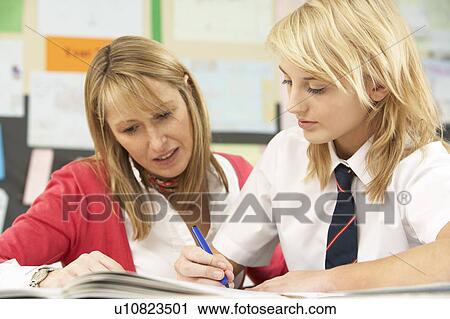 Stock Image - Female Teenage Student Studying In Classroom With Teacher. Fotosearch