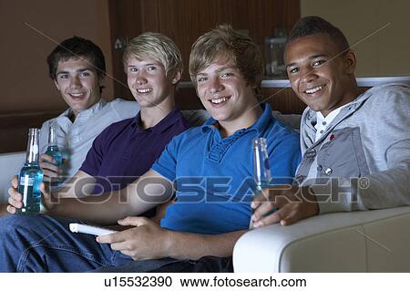 Stock Image - Group Of Teenage Boys Sitting On Sofa At Home Watching Drinking Alcohol. Fotosearch