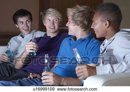 Stock Photo - Group Of Teenage Boys Sitting On Sofa At Home Watching Drinking. Fotosearch