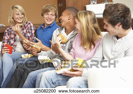 Stock Image - Group Of Teenage Friends Sitting On Sofa At Home Eating Fast Foo. Fotosearch
