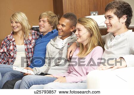 Stock Photo - Group Of Teenage Friends Sitting On Sofa At Home Watching TV. Fotosearch
