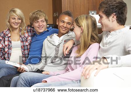 Stock Photograph - Group Of Teenage Friends Sitting On Sofa At Home Watching TV. Fotosearch