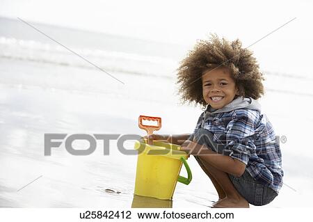 Stock Image - Happy boy at beach with bucket and spade. Fotosearch