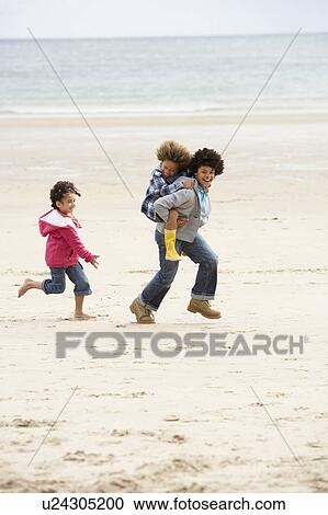 Stock Image - Happy children playing piggyback on beach. Fotosearch