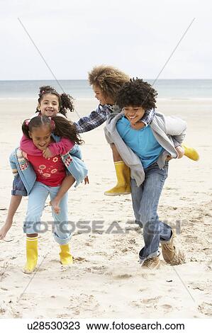 Stock Image - Happy children playing piggyback on beach. Fotosearch
