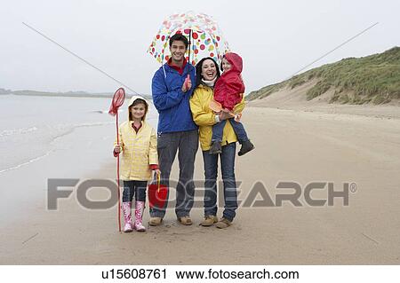 Stock Image - Happy family on beach with umbrella. Fotosearch
