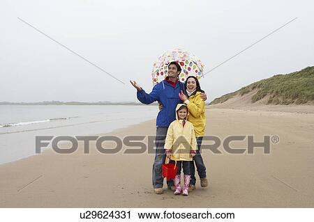 Stock Image - Happy family on beach with umbrella. Fotosearch