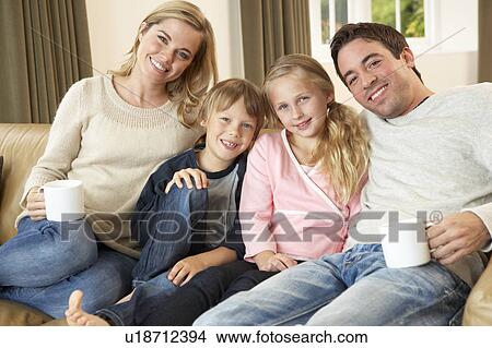Happy young family sitting on sofa holding cups View Large Photo Image Picture - Happy young family sitting on sofa holding cups. Fotosearch