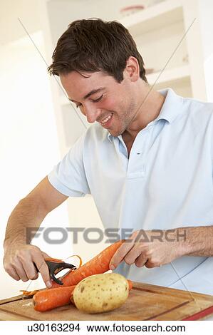 Happy young man peeling vegetable in kitchen View Large Photo Image Picture - Happy young man peeling vegetable in kitchen. Fotosearch
