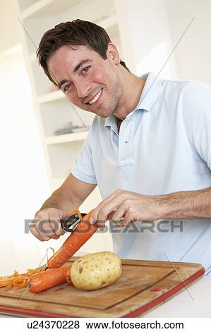 Happy young man peeling vegetable in kitchen View Large Photo Image Stock Photo - Happy young man peeling vegetable in kitchen. Fotosearch