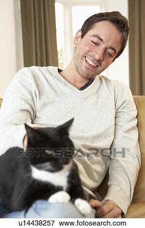 Stock Photo - Happy young man with cat sitting on sofa. Fotosearch
