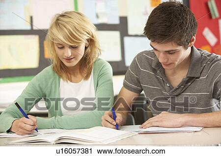 Stock Image - Male And Female Teenage Students Studying In Classroom. Fotosearch