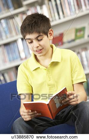 Stock Image - Male Teenage Student In Library Reading Book. Fotosearch