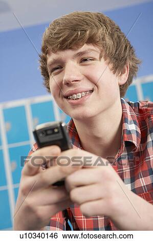 Stock Photograph - Male Teenage Student Using Mobile Phone By Lockers In School. Fotosearch