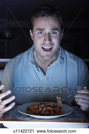 Stock Image - Man Enjoying Meal Whilst Watching TV. Fotosearch