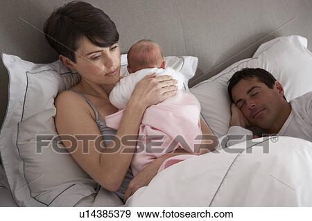 Stock Photo - Mother Cuddling Newborn Baby In Bed At Home. Fotosearch
