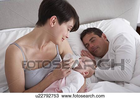 Stock Image - Mother Feeding Newborn Baby In Bed At Home. Fotosearch