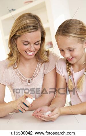 Stock Image - Mother putting sanitizer on young girl's hands. Fotosearch