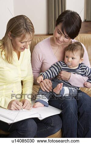 Stock Image - Mother With Baby Talking With Health Visitor At Home. Fotosearch