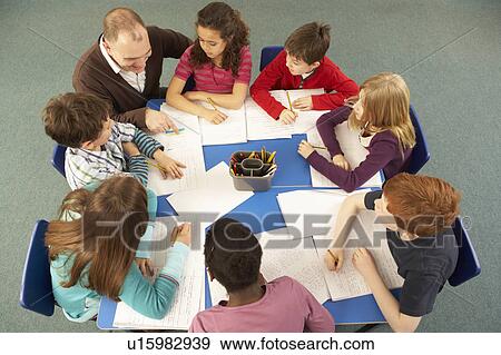 Stock Photo - Overhead View Of Schoolchildren Working Together At Desk With Teacher. Fotosearch