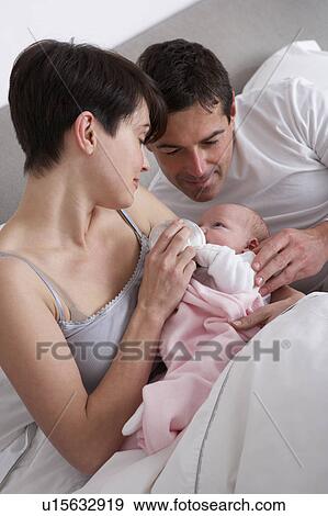 Stock Photo - Parents Feeding Newborn Baby In Bed At Home. Fotosearch