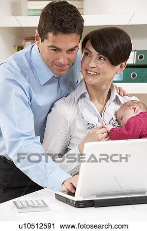Stock Image - Parents With Newborn Baby Working From Home Using Laptop. Fotosearch