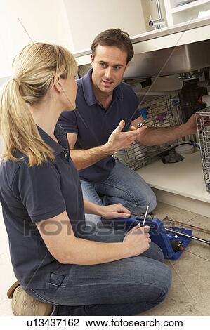 Stock Image - Plumber Teaching Apprentice To Fix Kitchen Sink In Home. Fotosearch