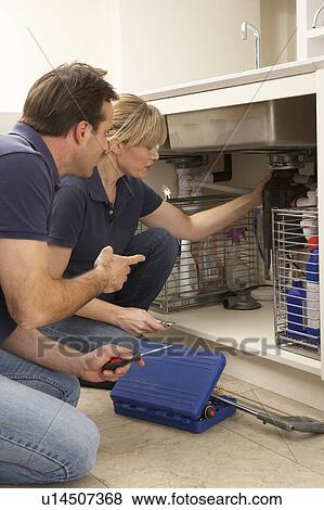 Stock Photo - Plumber Teaching Apprentice To Fix Kitchen Sink In Home. Fotosearch