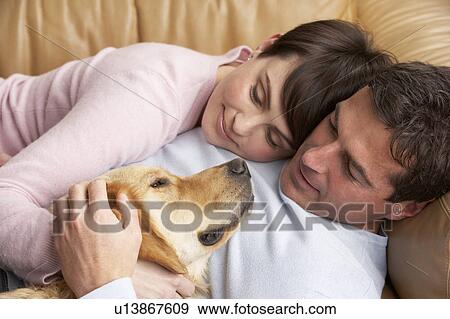 Stock Photo - Portrait Of Couple Relaxing On Sofa With Pet Dog At Home. Fotosearch