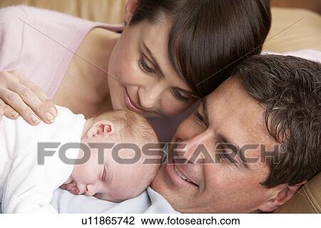 Stock Image - Portrait Of Proud Parents With Newborn Baby At Home. Fotosearch