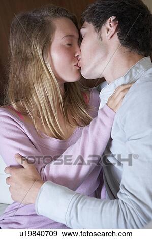 Stock Photo - Romantic Teenage Couple Kissing On Sofa At Home Together. Fotosearch