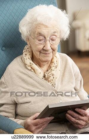 Stock Photo - Sad Senior Woman Looking At Photograph In Frame. Fotosearch